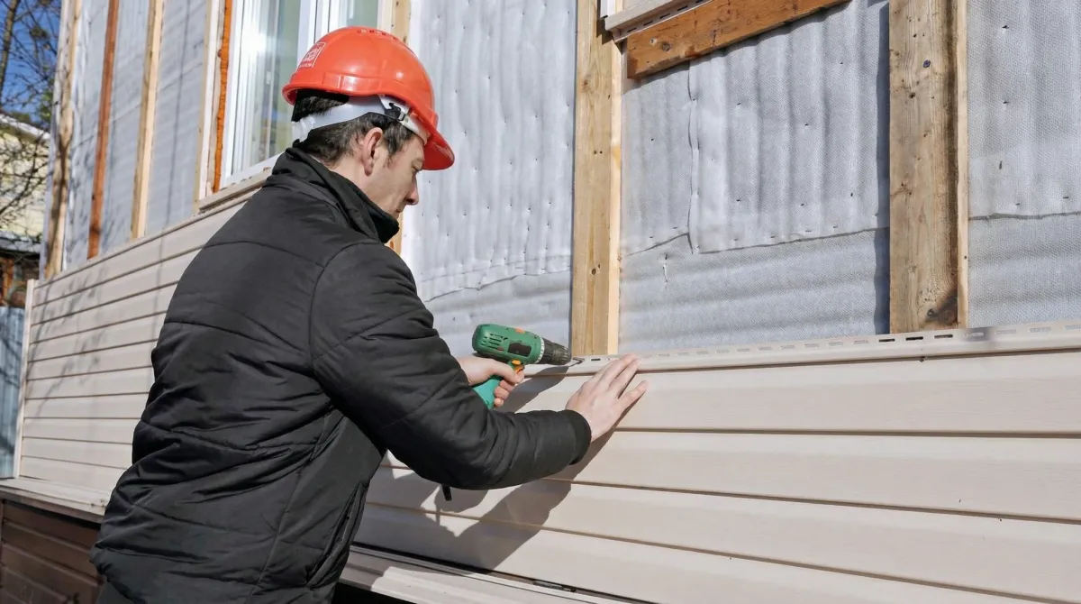Siding replacement professional using a power drill to install new tan vinyl siding on a home exterior in Pueblo, CO